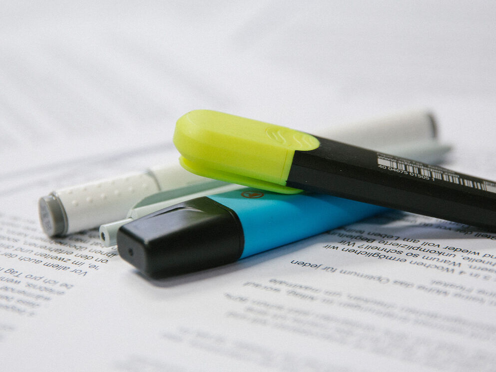 Neongelbe und cyanblaue Textmarker markieren entscheidende Textstellen auf einem Dokument – Symbol für das Schliessen von Wirkungslücken im Corpmedia Wirkungs-Assessment.