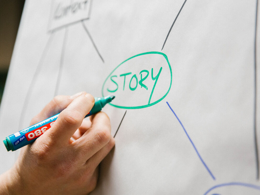 Wirkungsarchitekt Timo Wäschles Hand schreibt das Wort STORY mit einem grünen Textmarker auf ein Flipchart – Strategische visuelle Storyentwicklung bei Corpmedia.