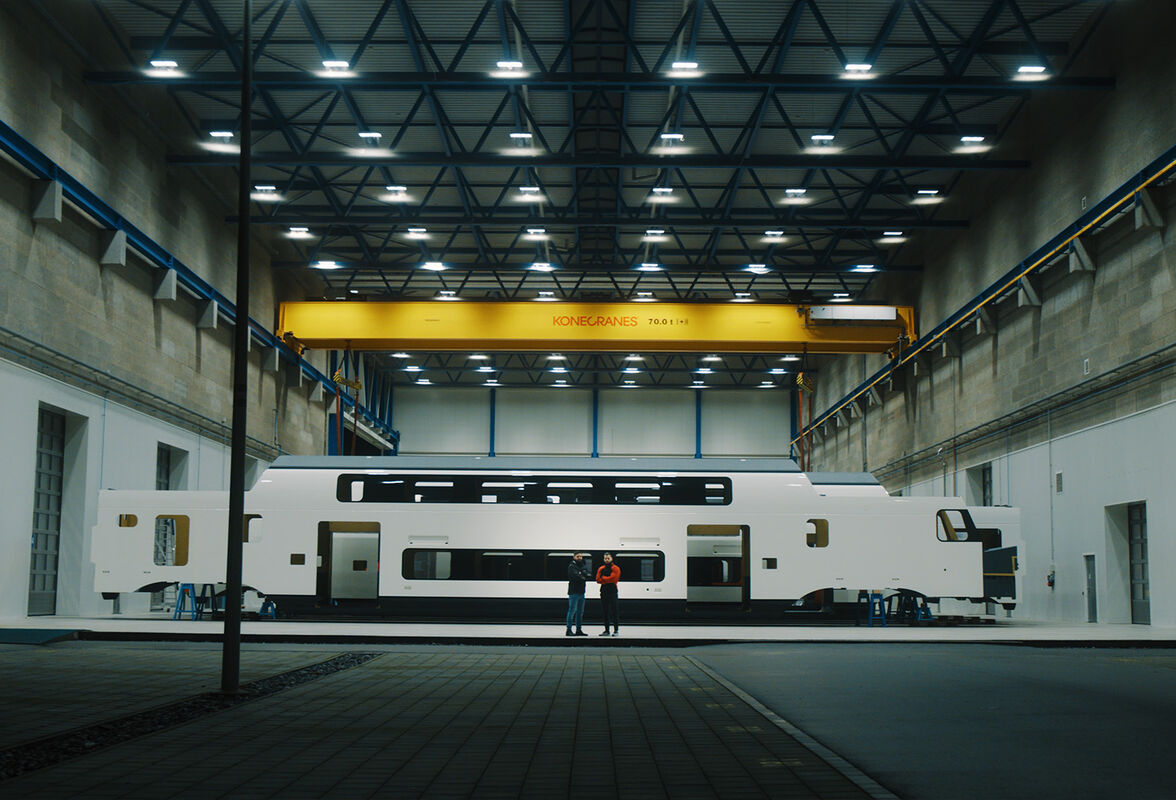 Filmstill aus dem Jungheinrich Stadler Rail Imagefilm – Leslie Tobler von Jungheinrich mit dem Stadler Rail Kunden im Abschlusshot vor einem Stadler Zug in der Produktionshalle, gedreht von CORPMEDIA mit 8.6K Kinokamera.