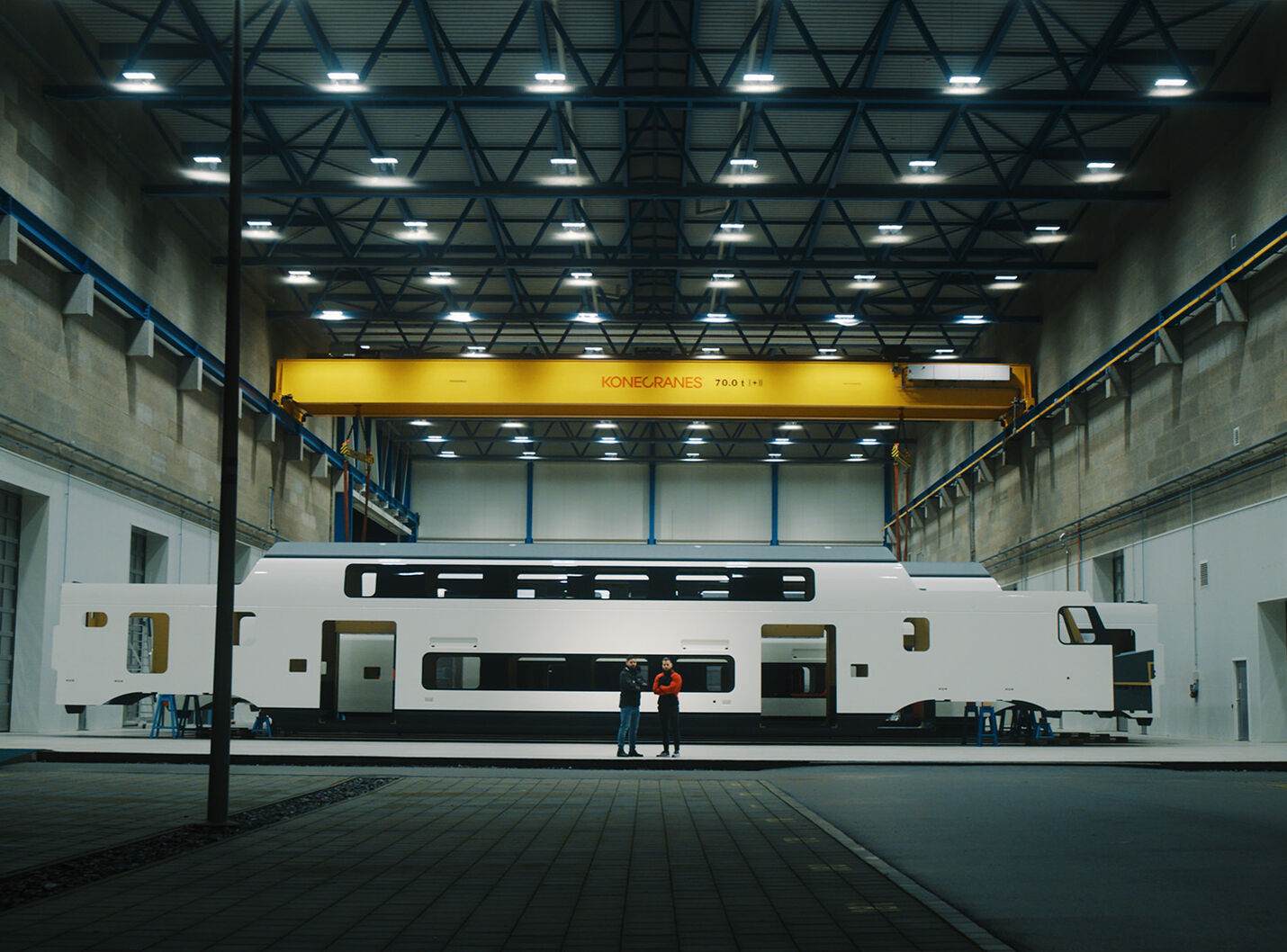 Filmstill aus dem Jungheinrich Stadler Rail Imagefilm – Leslie Tobler von Jungheinrich mit dem Stadler Rail Kunden im Abschlusshot vor einem Stadler Zug in der Produktionshalle, gedreht von CORPMEDIA mit 8.6K Kinokamera.