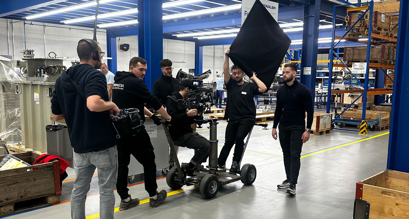 CORPMEDIA Filmcrew mit Regisseur Lars Badertscher, Sony Burano auf Dolly und Flag in der Stadler Rail Lagerhalle – Behind the Scenes des Jungheinrich Imagefilms, Employer Branding Produktion Schweiz auf Kinoniveau.