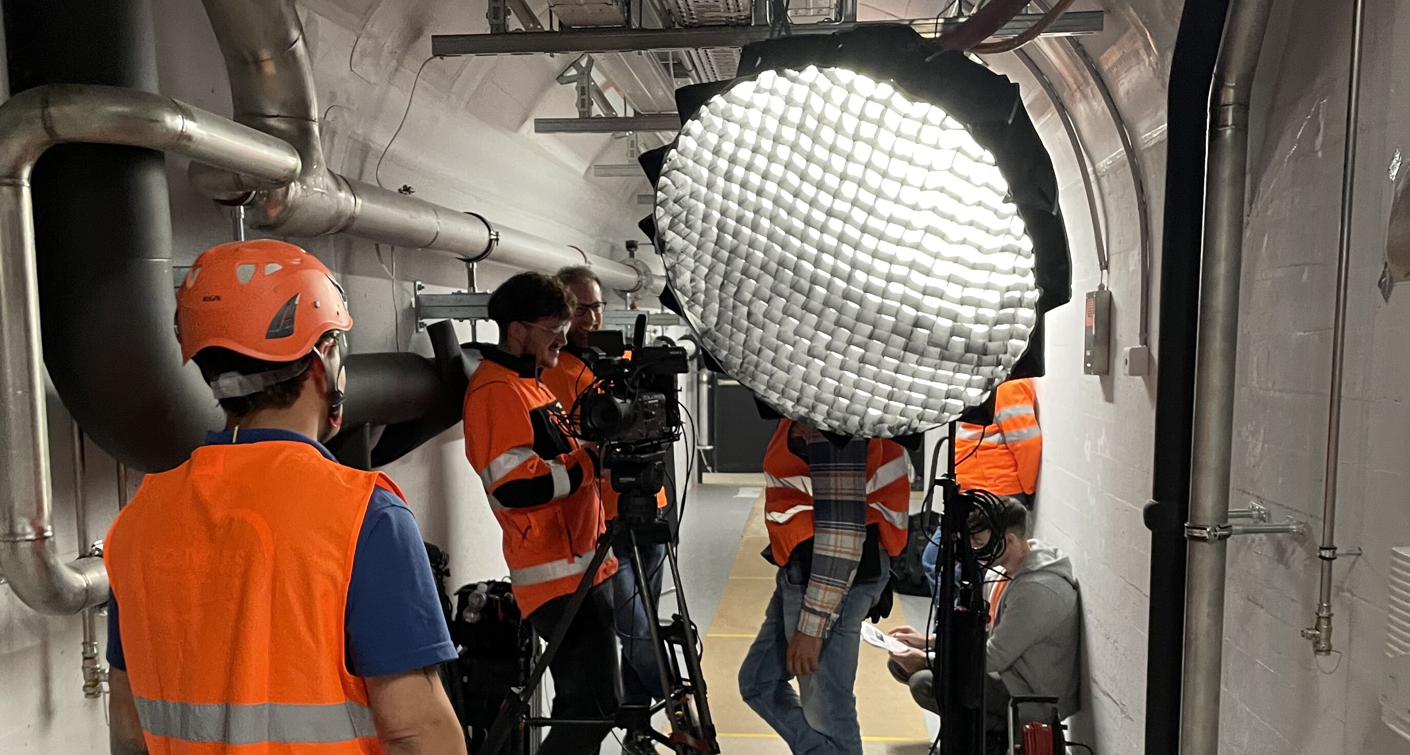 CORPMEDIA Filmcrew mit grossem Scheinwerfer im Rechenzentrum-Stollen Luzern – Imagefilm-Produktion für Bouygues und ewl, begleitet vom Sicherheitsbeauftragten, präzise und professionell umgesetzt unter laufendem Baubetrieb.