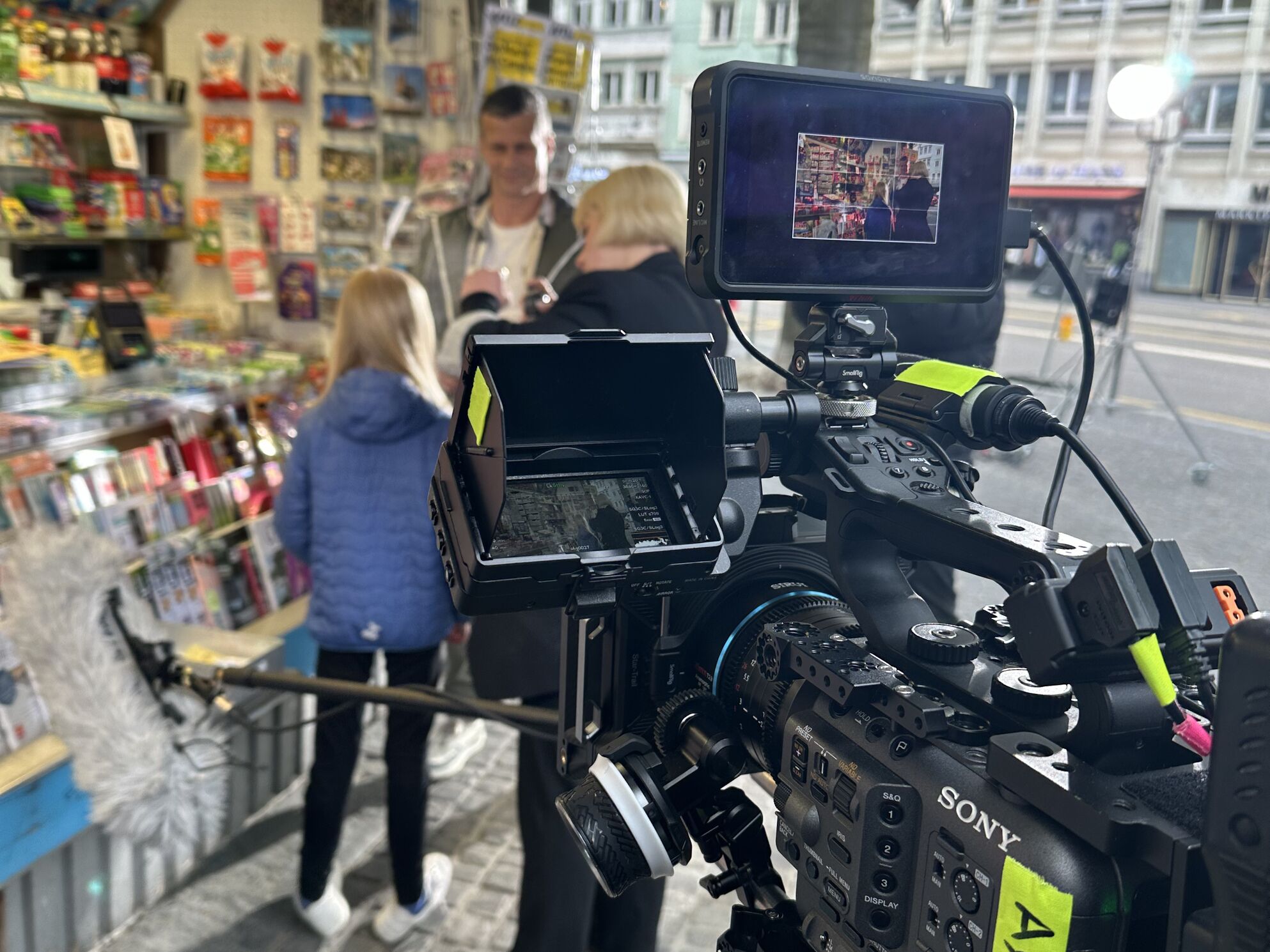 Behind the Scenes am Kiosk-Set des Kaspar& acrevis Kinospots – CORPMEDIA Filmcrew mit Sony Kamera beim Dreh der Szene, in der ein Götti seiner Nichte dank gespartem Wechselgeld ein Heftli kauft und als Überraschung ein iPhone findet.