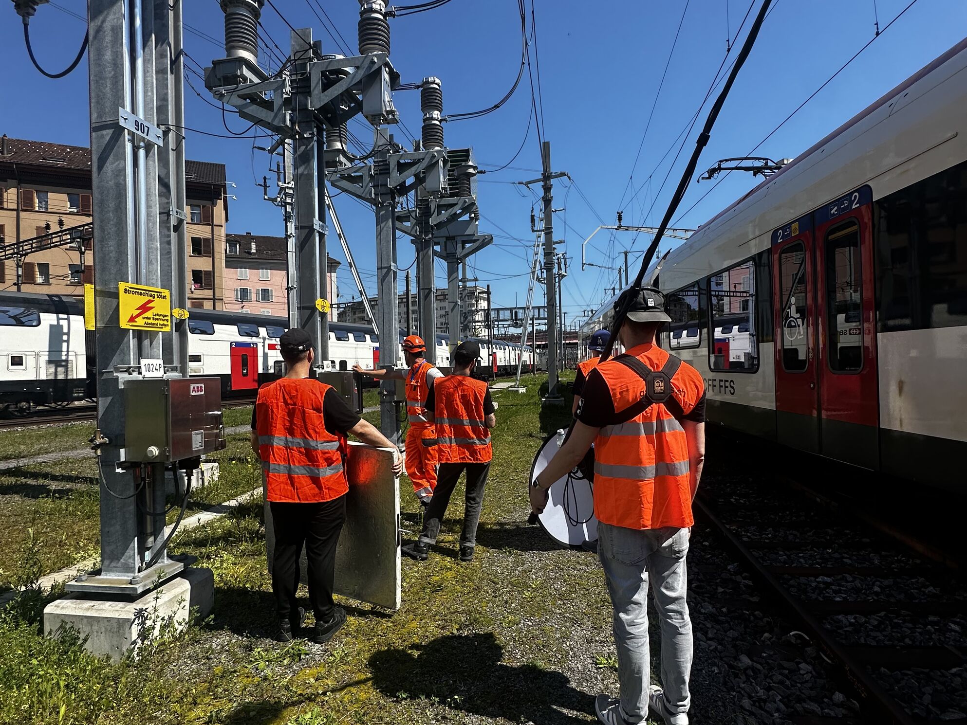 CORPMEDIA Filmcrew mit SBB Bahnstrom Team in orangenen Schutzwesten im Gleisbett in Luzern – Behind the Scenes des mehrsprachigen Employer Branding Films für SBB CFF FFS, gedreht an einem Tag an zwei Locations.